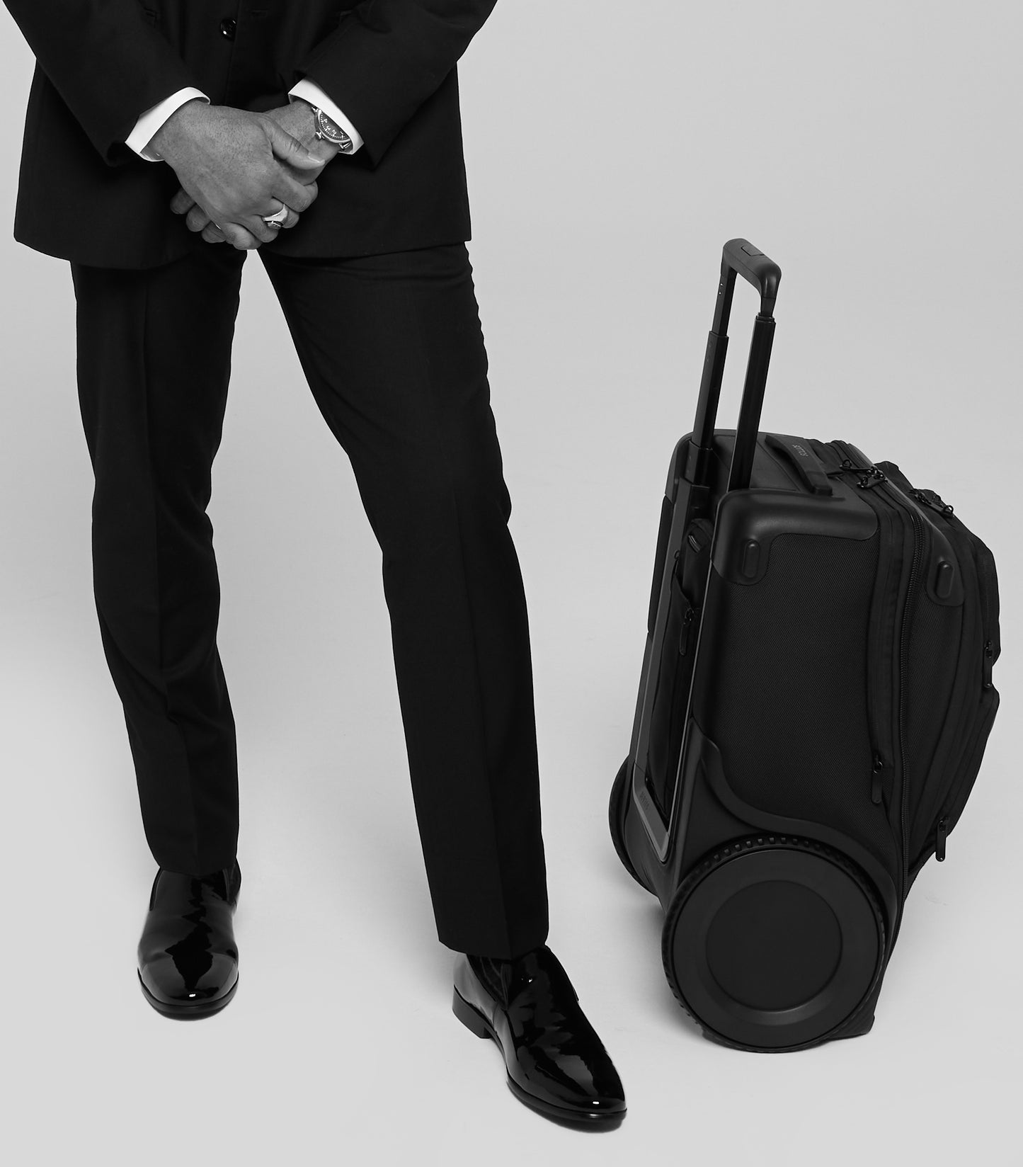 A business man standing at ease next to his SOTTOS Carry-On with black wheels.