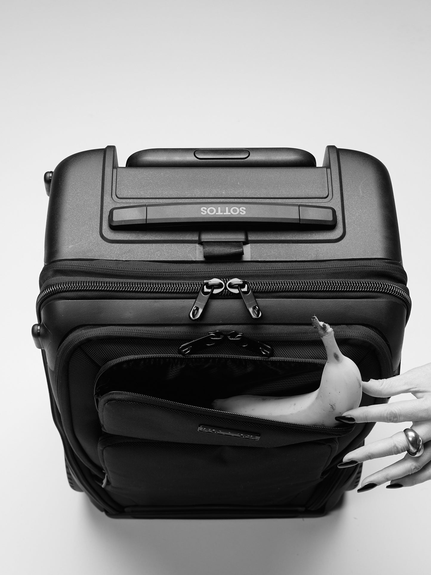 A woman's hand placing a banana in the top pocket of the SOTTOS luggage.